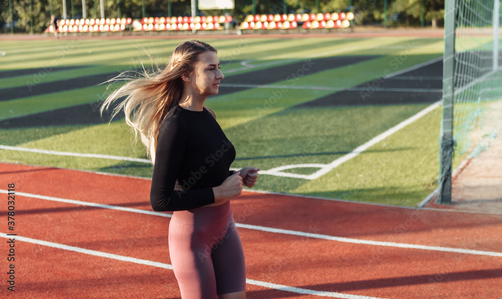 Attractive cheerful woman runs in the stadium. Healthy lifestyle concept. Morning running