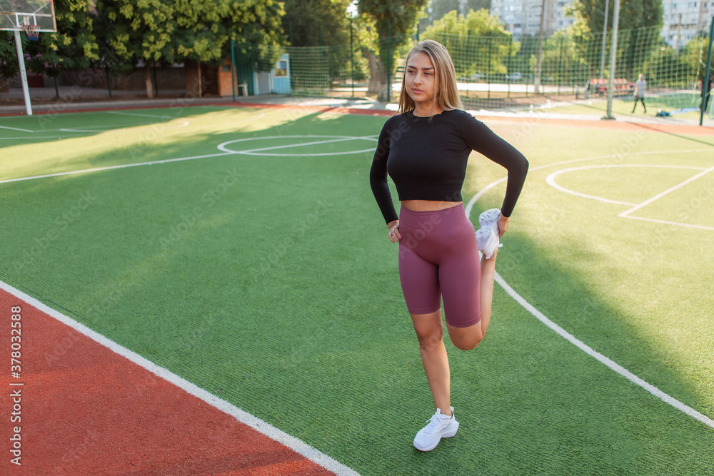 Young attractive woman in sportswear doing pre-training warm-up, legs stretching at the stadium. Healthy lifestyle concept. Outdoor training