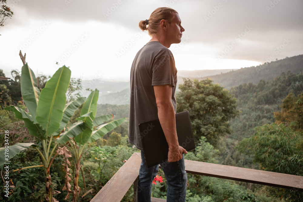 Fototapeta premium Young man freelancer hold in hands laptop and look at the mountains