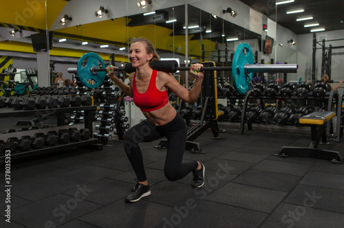 Young slim fit woman practicing lunges with a barbell on her shoulders in a modern gym