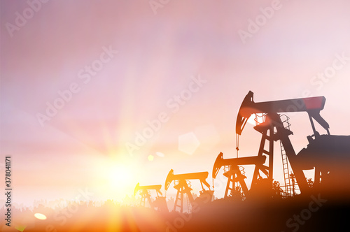 Dark silhouette of drilling rig and pump during sunset