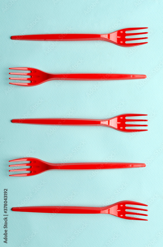 Vertical image.Top view of row of red plastic forks on the bright blue surface Vertical image.Top view of row of red plastic forks on the bright blue surface