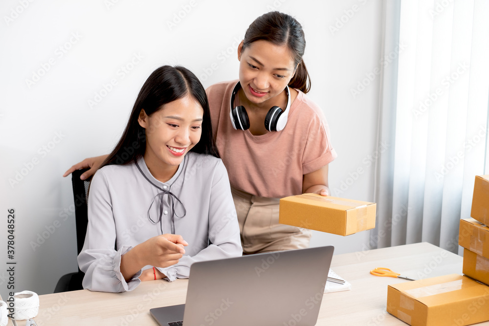 Asian woman business two people owner with many parcel boxes on the table happy online sales job, use your laptop, get an order from customers, take notes, and make arrangements for delivery by post Asian woman business two people owner with many parcel boxes on the table happy online sales job, use your laptop, get an order from customers, take notes, and make arrangements for delivery by post