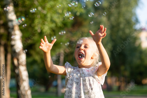 Little cute girl in the summer park blowing bubbles and having fun