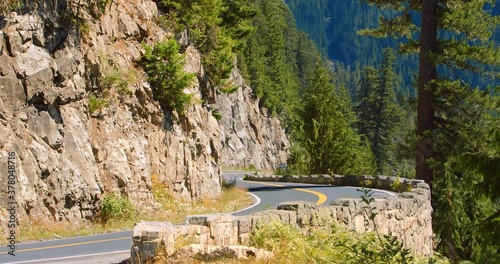 locked long shot of a curvy road on a mountain pass. yellow stone and rocks on one side and cliff on the other. in the distance faded trees 