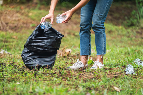 Closeup image of a female activist picking up garbage plastic bottles into a plastic bag in the park for recycling concept