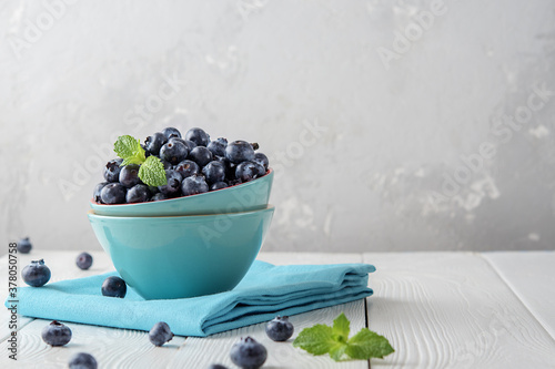 Fresh blueberries in a blue bowl on a light wooden table with copies of space.