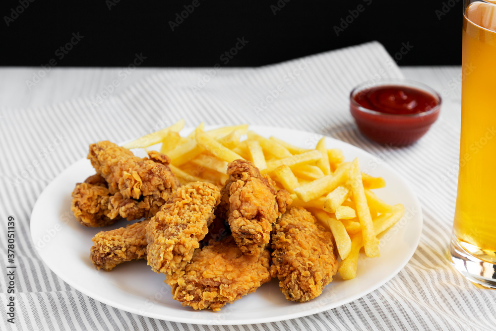 Homemade Crispy Chicken Wings and French Fries on a white plate, glass of cold beer, side view. Close-up. Homemade Crispy Chicken Wings and French Fries on a white plate, glass of cold beer, side view. Close-up.