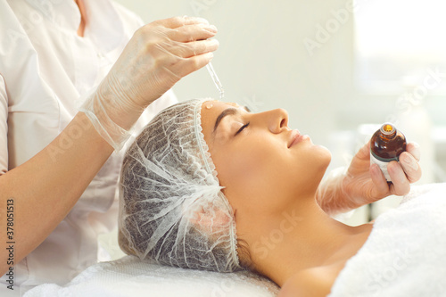 Professional cosmetician using pipette to apply moisturizing serum on client's face