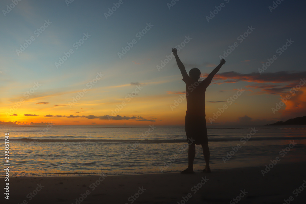A man raising arms  at sunset seaside beach  Success, celebrating goals and achievement.