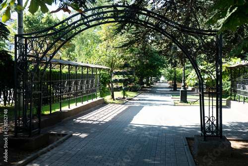 Metal semicircular arch in front of the alley in the summer park.