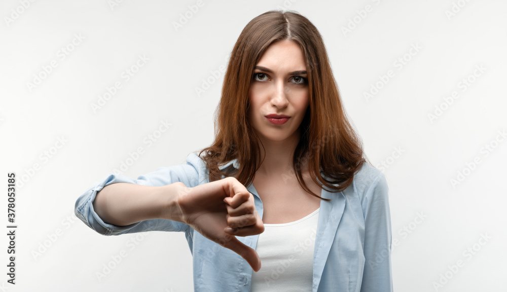 Photo of Beautiful girl in casual clothes, looking is upset at the camera, holding thumb down. Concept of dislike Photo of Beautiful girl in casual clothes, looking is upset at the camera, holding thumb down. Concept of dislike