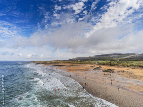 Aerial drone view on Fanore beach, county Clare, Ireland. Warm sunny day, People on the beach and surfing in the water. Cloudy sky, Popular surfing spot. photo