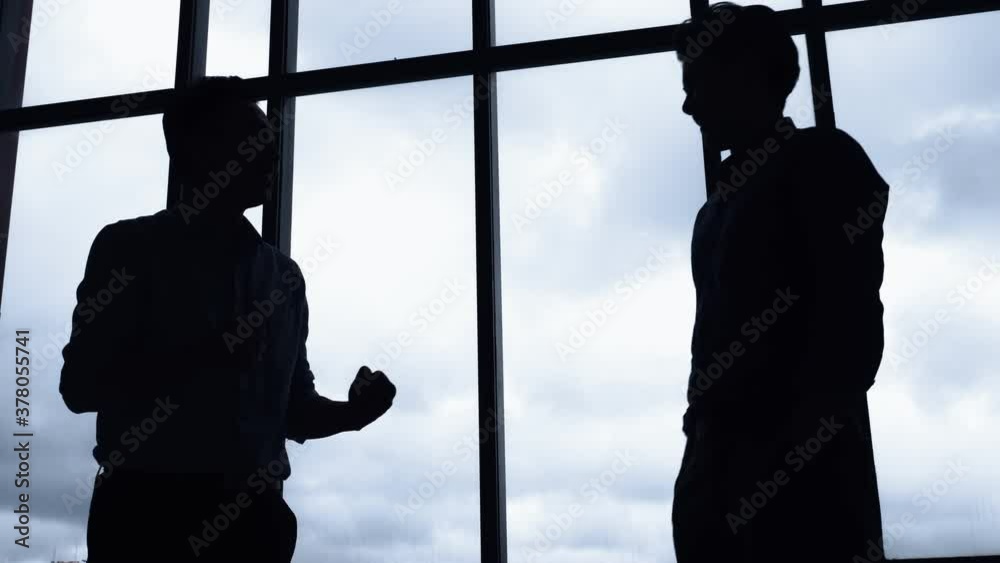 Silhouettes of two businessman shaking hands in the office.
