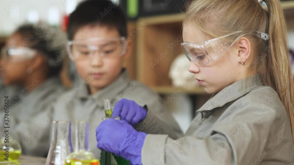 Laboratory experience in a chemistry lesson, girl and asian boy in protective glasses holding a flasks with a liquids in hands, modern education at school, children view liquids in flasks. Laboratory experience in a chemistry lesson, girl and asian boy in protective glasses holding a flasks with a liquids in hands, modern education at school, children view liquids in flasks.