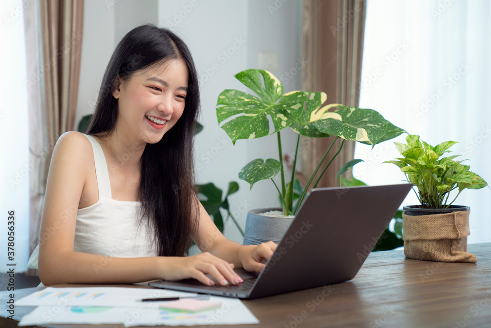Asian girl typing data to her computer notebook for prepare her report on the wooden deak with the green plant on the table, this image can use for education, office, university and student concept. Asian girl typing data to her computer notebook for prepare her report on the wooden deak with the green plant on the table, this image can use for education, office, university and student concept.