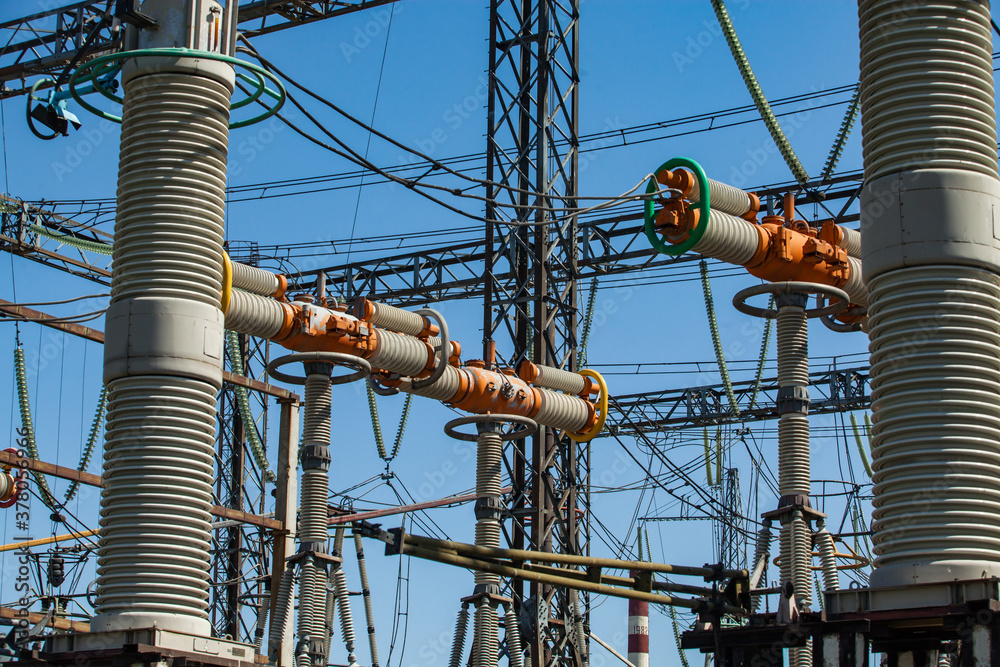 Power generating plant. Transformer substation on blue factory building and sky background. Orange high-voltage switcher and equipment close-up. Power generating plant. Transformer substation on blue factory building and sky background. Orange high-voltage switcher and equipment close-up.