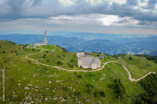 Drone panorama of Top of Urslja gora or Plesivec in the Koroska region of slovenia on a summer day. Visible grass, church of st. Ursula, and TV antenna on the top, with Pohorje mountains in the backgr photo