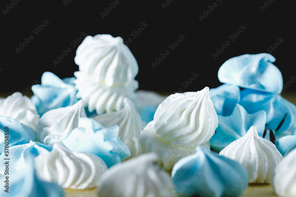 white and blue meringue in the form of drops, lies on a brown table on a black background. Side view.