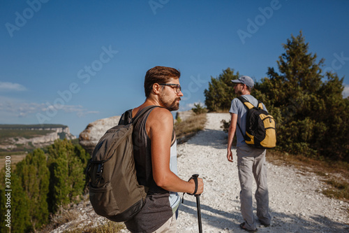 Two Men walking on rocky slope carrying Backpacks using trekking Sticks.