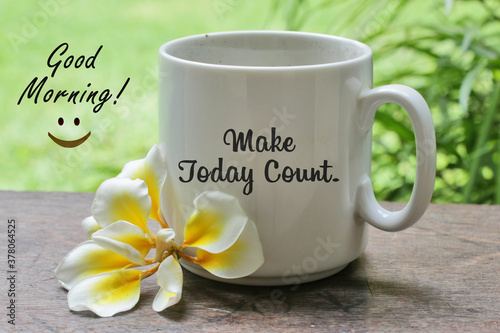 A cup of coffee with Bali frangipani flower on the wooden table with inspirational motivational quote on it - Make today count. With good morning  text greeting and an happy smiling sign.