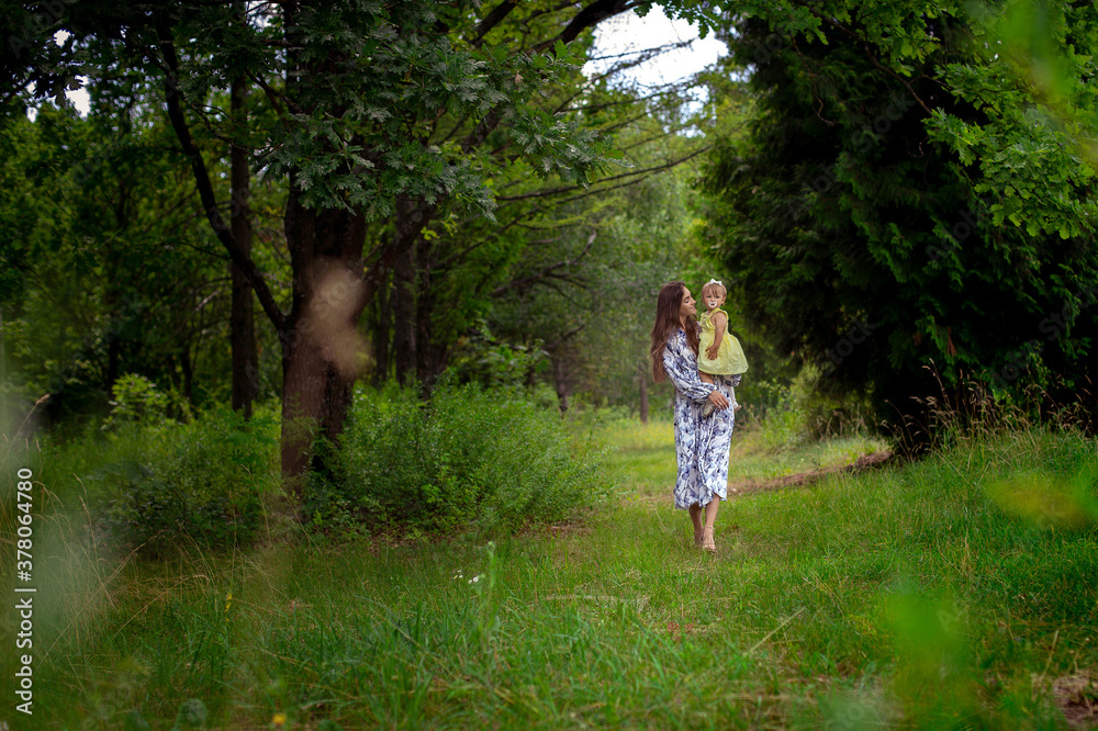 beautiful young woman walks carrying little baby girl at the garden