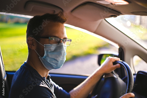portrait of attractive nerd in long sleeve glasses and protective face mask in electric car at sunset