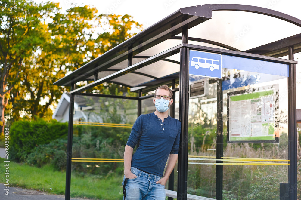 portrait of attractive nerd in long sleeve glasses and protective face mask next to the bus stop at sunset portrait of attractive nerd in long sleeve glasses and protective face mask next to the bus stop at sunset