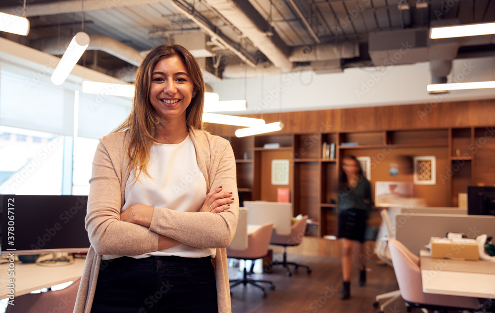 Portrait Of Smiling Businesswoman Standing In Busy Modern Open Plan Office Portrait Of Smiling Businesswoman Standing In Busy Modern Open Plan Office