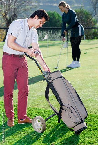Male golfer examining clubs while his female golf partner hitting ball