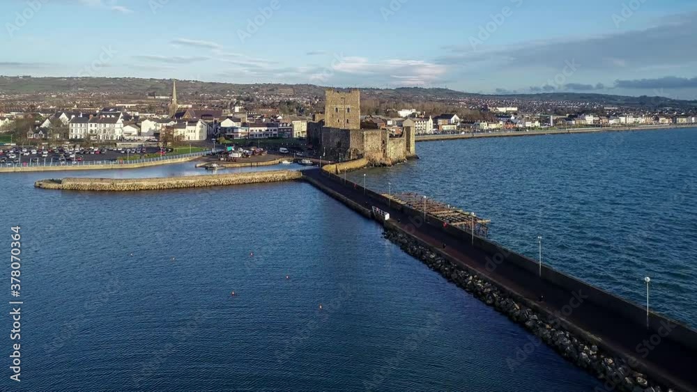 Medieval Norman Castle and harbor in Carrickfergus near Belfast in sunrise light. Aerial 4K approaching video with marina, boat ramp, breakwater and town