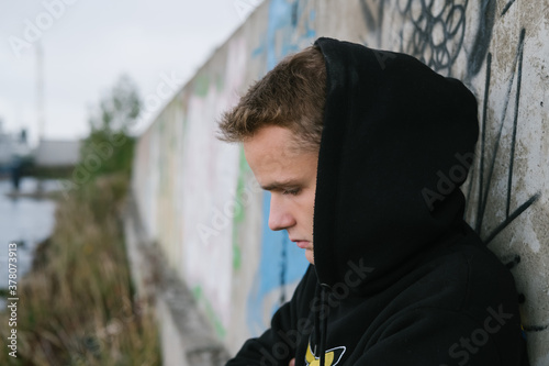 Obraz na płótnie portrait of a sad lonely teenager / young guy in a black hoodie in an abandoned place near the port w salonie