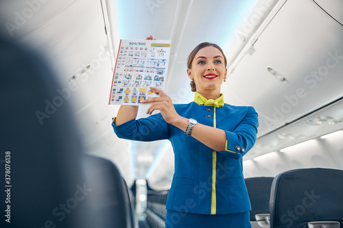 Smiling cheerful air hostess in blue uniform showing to passenger safety information photo