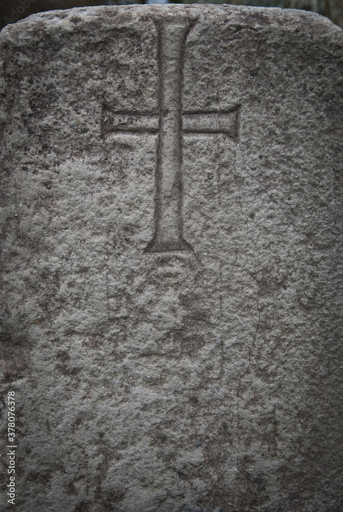 Simple cross carved in stone.  Modest christian symbol on an old sandstone grave. 