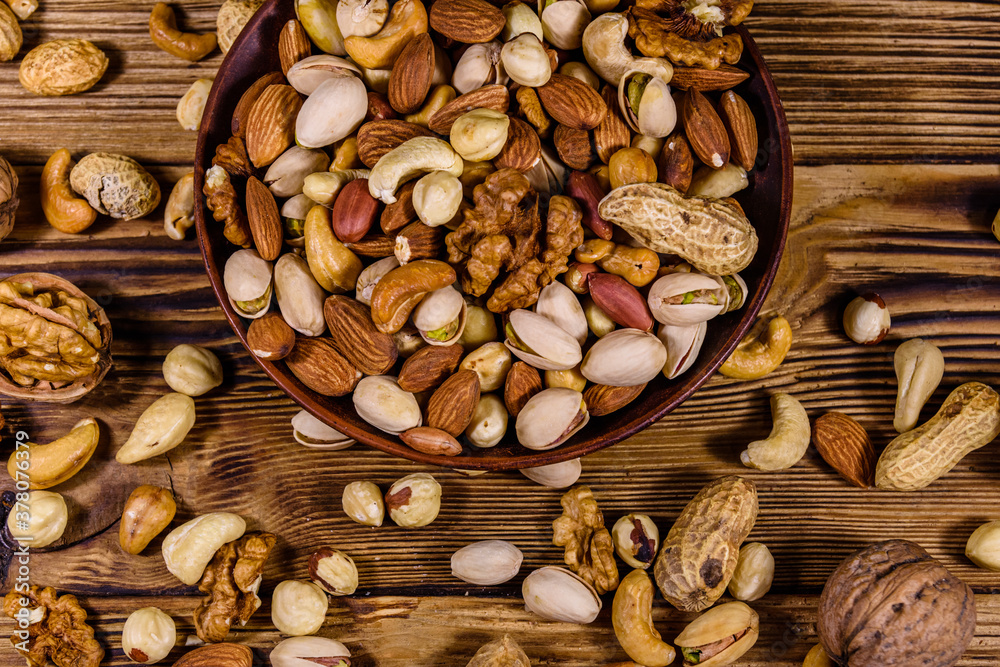 Various nuts (almond, cashew, hazelnut, pistachio, walnut) in ceramic plate on a wooden table. Vegetarian meal. Healthy eating concept. Top view