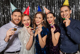 celebration, fun and holidays concept - happy couple with party blowers and birthday caps