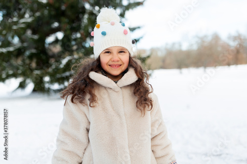 childhood, leisure and season concept - portrait of happy little girl in winter clothes outdoors at park