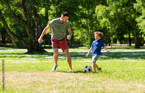 family, fatherhood and people concept - happy father and little son with ball playing soccer at summer park