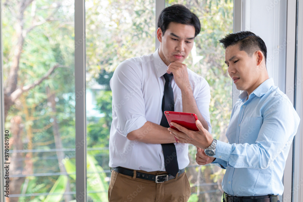 Two businessmen working at the office. Serious coworkers holding using digital tablet discussing corporate strategy with device in modern office. Two business people discussing something seriously. Two businessmen working at the office. Serious coworkers holding using digital tablet discussing corporate strategy with device in modern office. Two business people discussing something seriously.