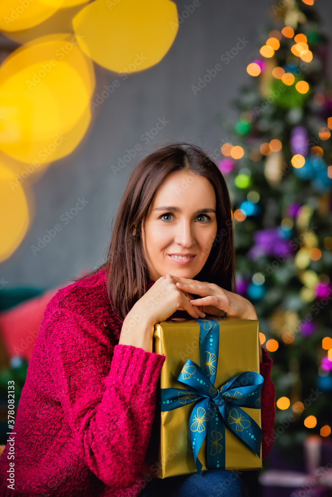 Portrait of a dark-haired girl with a gift on the background of a Christmas tree. Portrait of a dark-haired girl with a gift on the background of a Christmas tree.