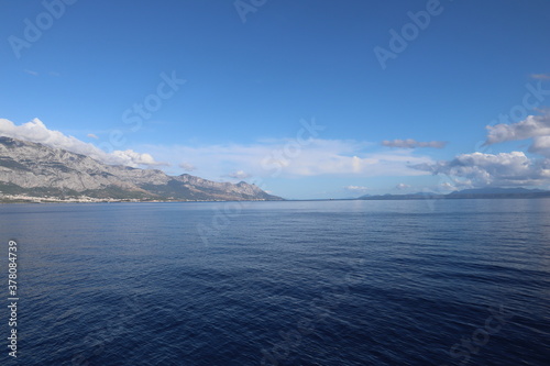 Seascape on the Croatian coast view from the sea on a sunny day. A scenic view of the coastline of the mountain range and island against the backdrop of the blue sea and clear sky on a September day