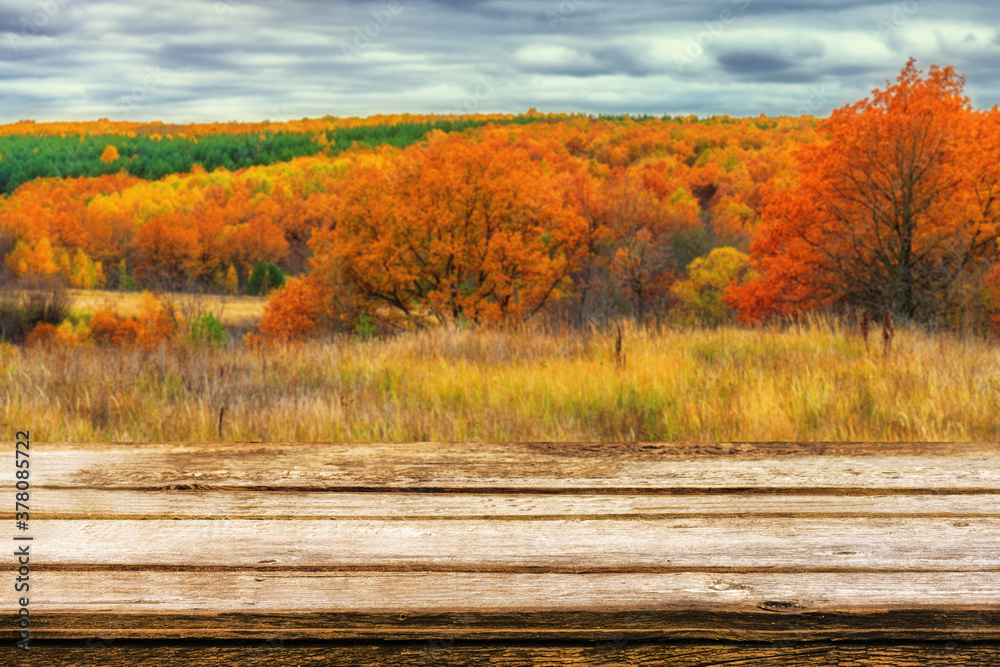 Empty wooden table with blurred picturesque autumn landscape of panoramic view from hill to lowland with field and grove in cloudy day. Mock up for display or montage products Empty wooden table with blurred picturesque autumn landscape of panoramic view from hill to lowland with field and grove in cloudy day. Mock up for display or montage products