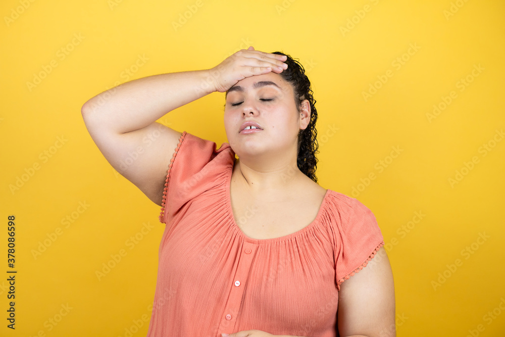 Young beautiful woman with curly hair over isolated yellow background putting one hand on her head smiling like she had forgotten something Young beautiful woman with curly hair over isolated yellow background putting one hand on her head smiling like she had forgotten something