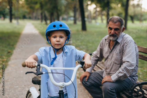 boy riding bicycle with his grandfather at the city park