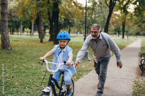 boy riding bicycle with his grandfather at the city park