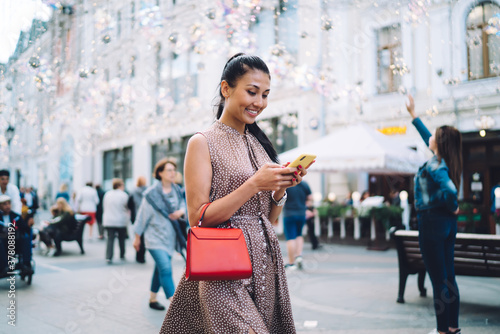Happy Asian woman with digital smartphone technology chatting while walking in touristic city enjoying summer vacations for travelling, cheerful millennial girl with cellphone writing email message