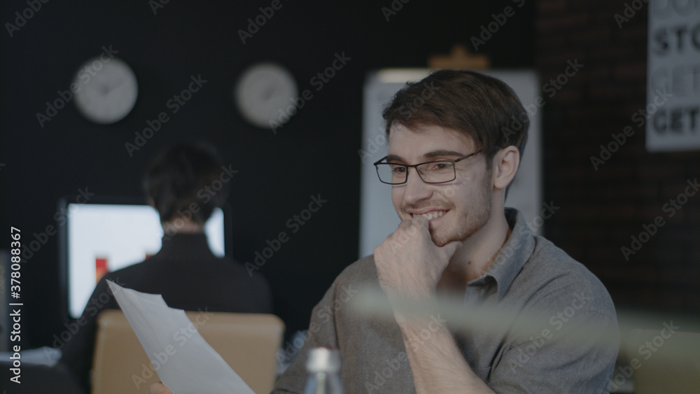 Smiling business man looking document paper on workplace in dark office