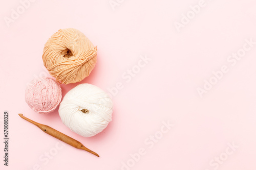 White and brown knitting wool and crochet hook on pink pastel background. Top view, flat lay, copy space