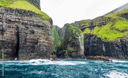 Gloomy Vestmanna cliffs near the ocean with long waterfall photo