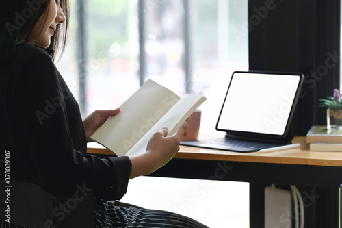 Cropped image of woman reading book while using taplet search information.